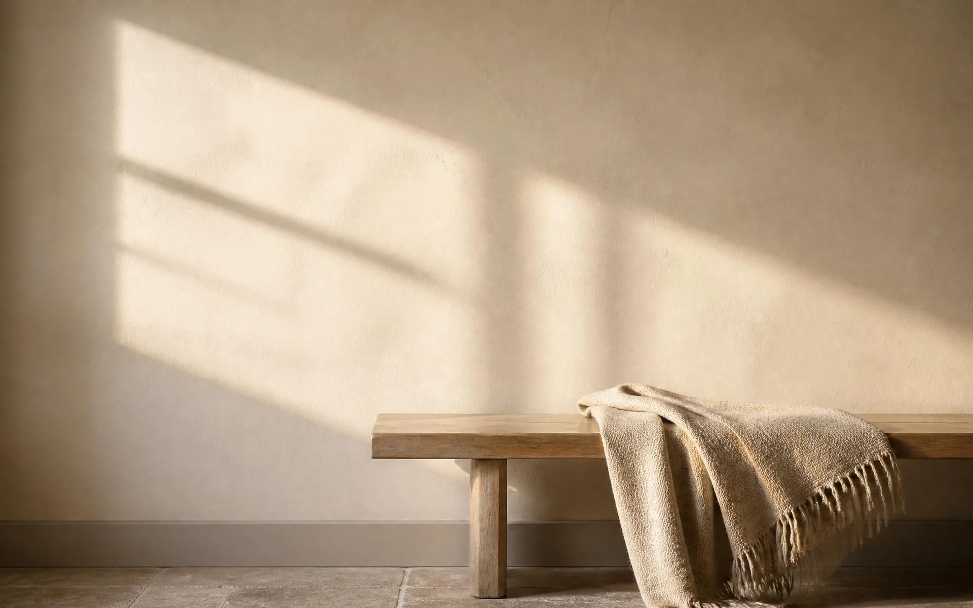 A wooden bench and folded linen throw in soft morning light